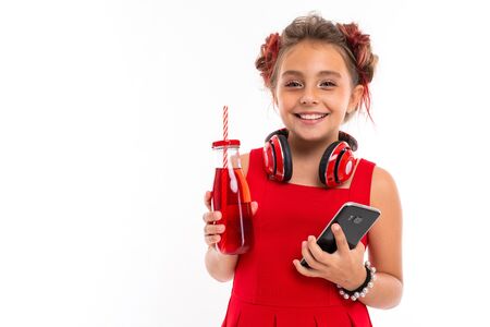 Nice girl in red dress with big earphones drinks juice isolated on white background.の写真素材