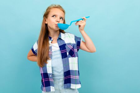 smiling european girl tastes with a spoon in her hands on a light blue background.の写真素材