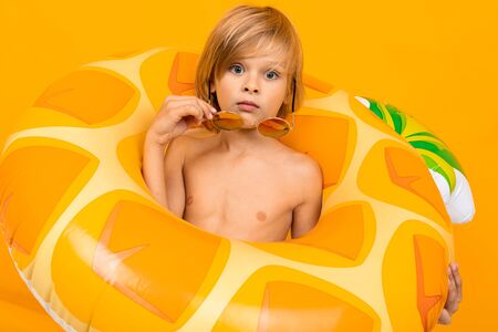 Portrait of pretty european blond boy in yellow swimming trunks and sunglasses with a pineapple...