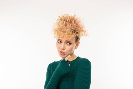 attractive curly blonde girl in a green sweater with arms crossed on a white background.