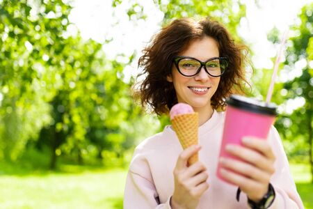 Pretty young caucasian woman go for a walk at park with coffe and ice-cream.
