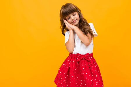 Caucasian girl in a skirt shows that she wants to sleep on a yellow background.の写真素材