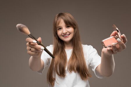 Caucasian teenager do makeup with brushes isolated on brown background.の写真素材