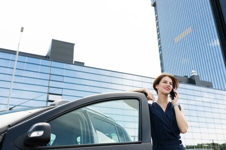 Caucasian woman in strict style of clothing, red lips, short haircut gets out of the car for an...