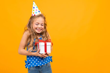 smiling girl in a holiday hat holds a gift box on an orange studio background with copy space.の写真素材