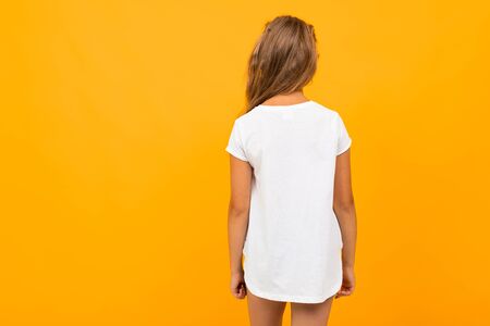 girl stands with her back in a white T-shirt with a mockup on an orange background.の写真素材
