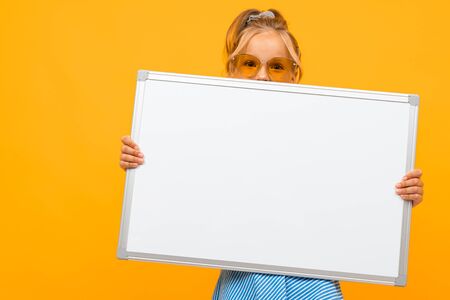 stylish young girl holding a white board with a mockup on a yellow background.の写真素材