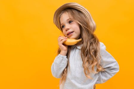 Portrait of pretty caucasian girl with hat holds gesticulates with banana isolated on yellow...