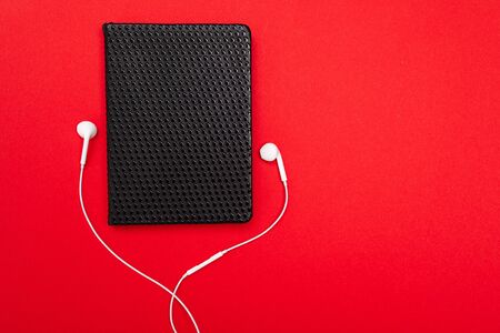 Black notebook with white earphones isolated on red background.の写真素材