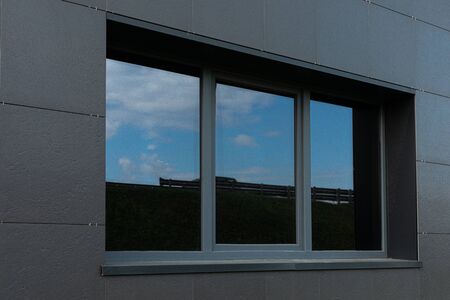 Black wall and big windows of tall building with sky reflection.