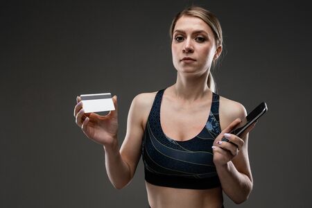 slim girl in sportswear with a credit card with a mockup and a phone on a black background.の写真素材