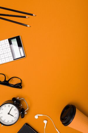 School and office supplies such as note, pens, pencils, calculator, brush, scissors, coffee, laptop lie neatly on an orange backgroundの写真素材