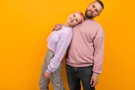 Unusual pretty woman with short pink hair and tattoo enjoys life with her boyfriend isolated on orange background.の写真素材