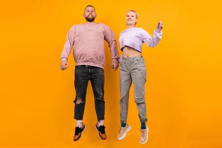 Unusual pretty woman with short pink hair and tattoo having fun with her boyfriend isolated on orange background.の写真素材