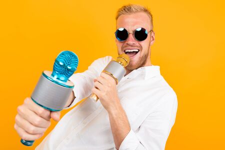 Fashionable caucasian male with glasses sings songs in karaoke isolated on yellow background