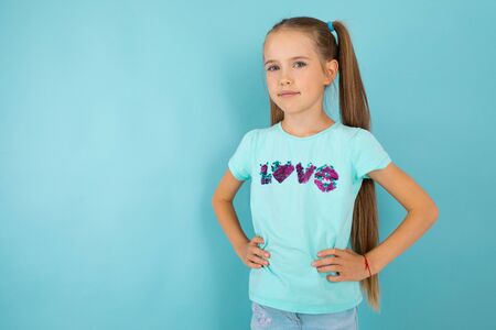 Fashionable teenager girl in blue t-shirt gesticulates and smiles, portrait isolated on blue backgroundの写真素材