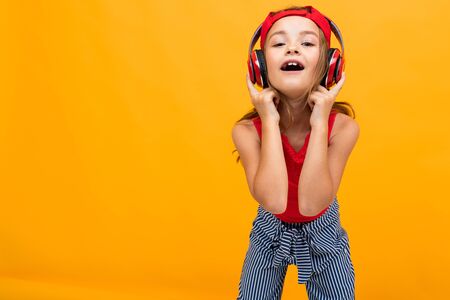 portrait of a beautiful charming young girl in a casual look with red headphones comes off to music on a yellow background with copy space.の写真素材