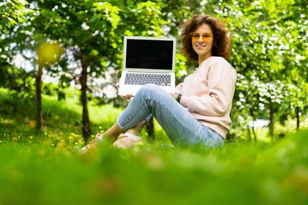 girl sitting on the grass in a summer park holding a laptop with the screen forward with the layout.
