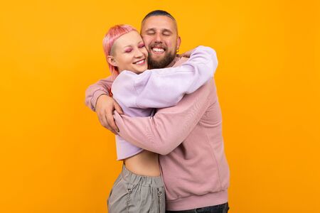 Unusual pretty woman with short pink hair and tattoo enjoys life with her boyfriend isolated on orange backgroundの写真素材