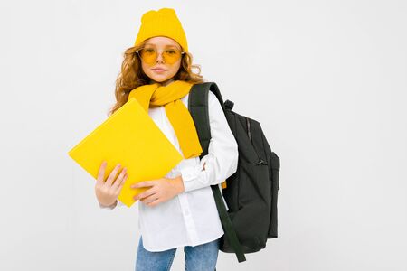 stylish caucasian charming schoolgirl in a white shirt, with a hat and a backpack with a notebook in...