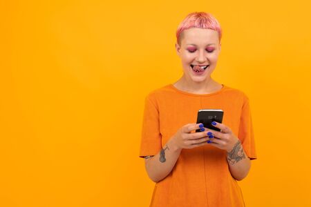 Extraordinary beautiful woman with short pink hair and big tattoo on her hand smiles isolated on orange backgroundの写真素材