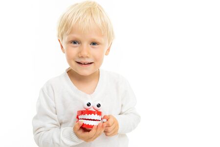 close-up of a blond male child with a toy in the form of a white tooth jaw on a white background...