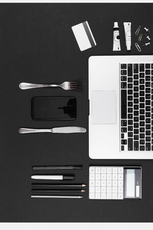 Fork, knife, laptop, calculator, pens, pencils, card, phone isolated on black backgroundの写真素材