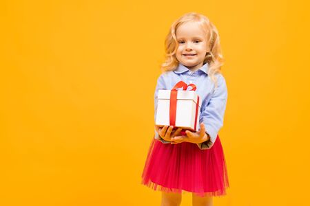 holiday concept. little girl with a gift on a bright yellow background.の写真素材