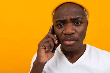Portrait of a handsome pensive serious American man in a white T-shirt talking on the phone on a...