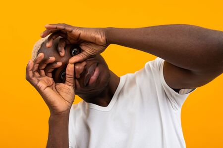surprised black african young man covers his face with his hands and bulges his eyes.