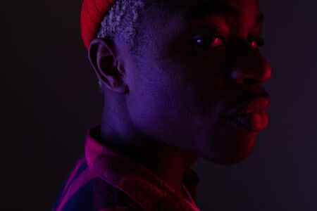 Closeup portrait of a dark-skinned American with big lips standing sideways in neon light.の写真素材