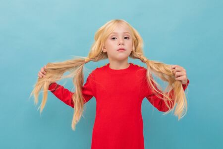 A little beautiful girl with long blonde hair braided in tails isolated on blue background.の写真素材