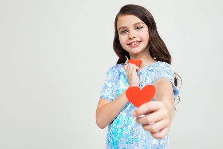 caucasian young girl holds two cards in the shape of a heart for valentines day on a light background with copy space.の写真素材
