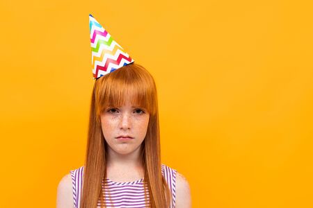 Sad young girl in purpe t-shirt with red hair isolated on yellow background.