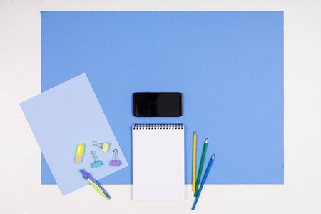 Mobile phone, notes, pens, pencils, ruler, eraser, compass isolated on blue and white background