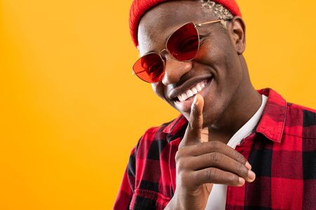 stylish smiling black african guy in red retro glasses on orange background with copy space.