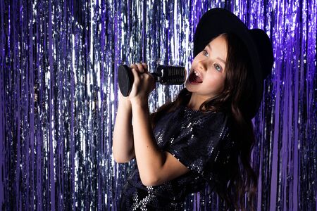 attractive european young girl singing with a microphone at a party against a background of black balloons and tinsel.の写真素材