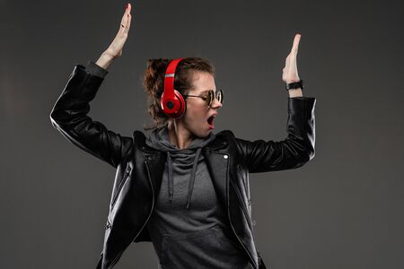 Portrait of beautiful caucasian female in grey hoodie, black jacket, black sunglasses listens to...