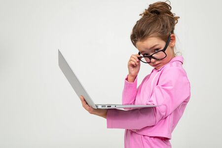 surprised attractive girl in a pink suit reads the news on a laptop on a white studio background.