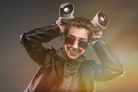 Portrait of beautiful caucasian female in grey hoodie, black jacket, black sunglasses listens to...