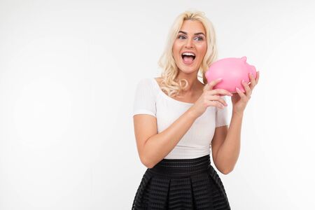 emotional wonderful girl with white hair in a classic white T-shirt holds a piggy bank on a white background with copy space.の写真素材