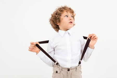 Caucasian pretty boy with curly hair in white shirt with black suspenders stands isolated on white backgroundの写真素材