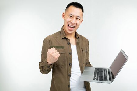 smiling happy asian man holding a laptop in his hands on a white studio background.の写真素材