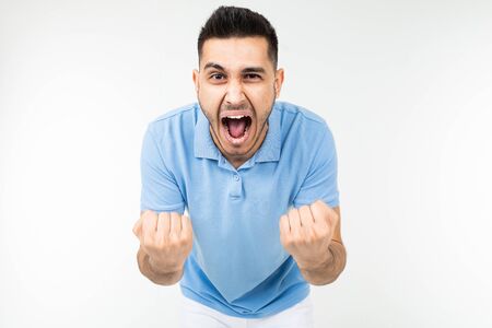 handsome caucasian man in a blue t-shirt holds fists for good luck on a white studio background.