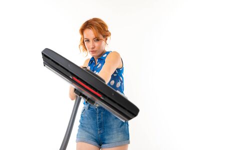 Portrait of caucasian female with fair red hair, pretty face in blue t-shirt and shorts with vacuum cleanerの写真素材