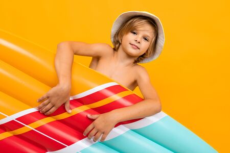 attractive European blond boy in a summer panama with an inflatable swimming mattress on a yellow background.の写真素材