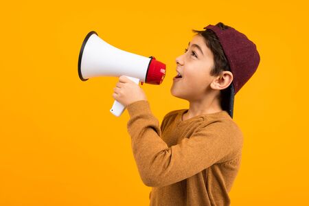 attractive european boy shouting news in a megaphone for a poster on an orange studio background.の写真素材