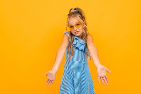 cute european girl in bright sunglasses shrugs on a yellow background.の写真素材