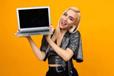 smiling young woman holding a laptop with a blank screen to insert a web page on a yellow studio backgroundの写真素材