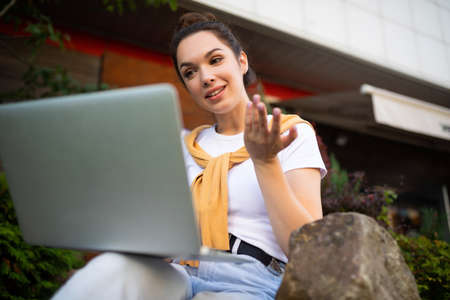 woman student studying on the street sitting with a laptop on her lap.の写真素材